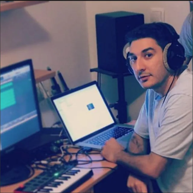Lolo Tof at work in a home studio, in headphones, between a laptop and a keyboard